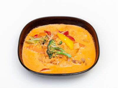 Azjatycka potrawa składająca się z żółtego wywaru, mięsa, brokuła i innych warzyw, podana w brązowej misce.