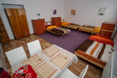Pokój z 4 łóżkami, fioletowym dywanem, szafkami i stołem z krzesłami.