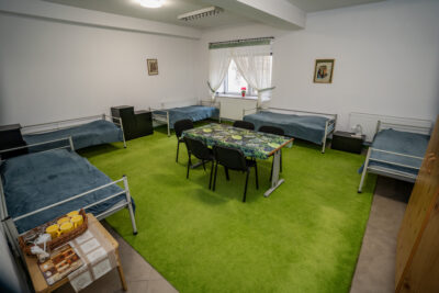 Pokój z pięcioma łóżkami, zielonym dywanem i stołem na środku.