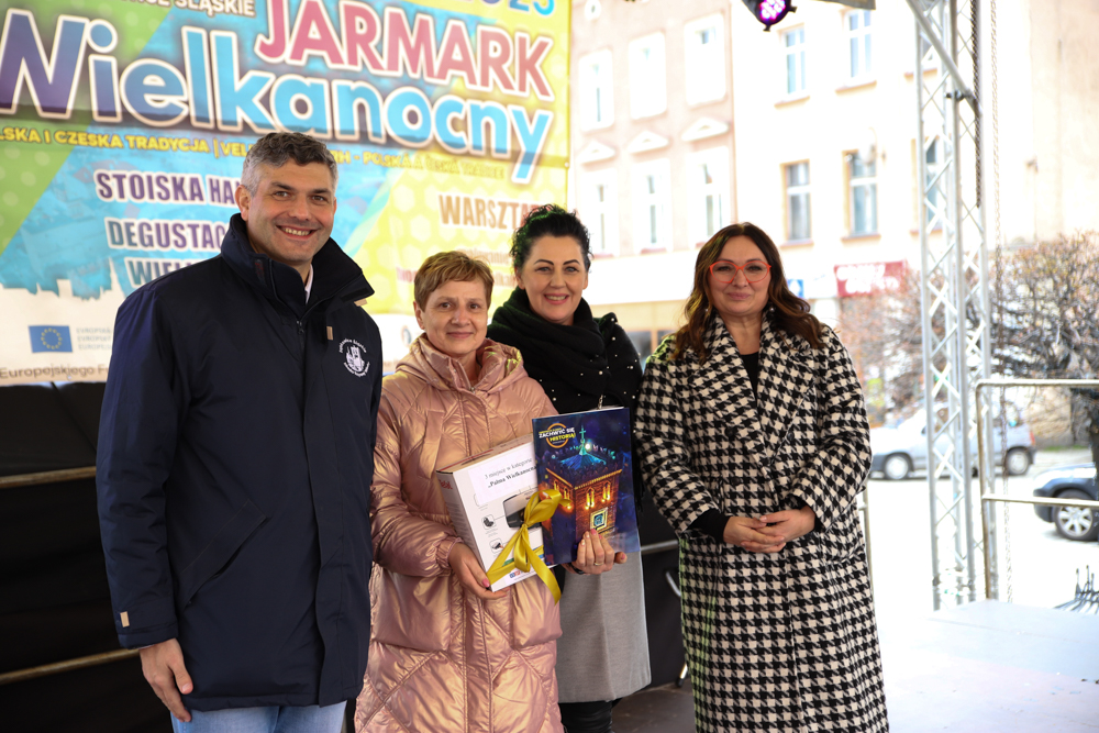 Rynek w Ząbkowicach Śląskich. Pod sceną stoi burmistrz Ząbkowic Śl. Marcin Orzeszek wraz z trzema kobietami.